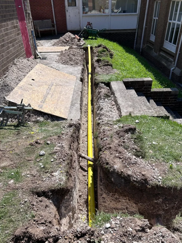 Yellow gas supply pipe in a deep excavation running alongside a brick building