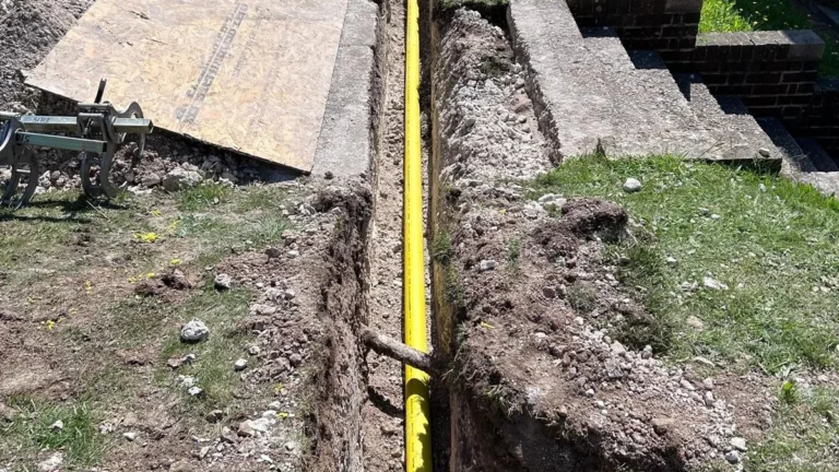 Yellow gas supply pipe in a deep excavation running alongside a brick building