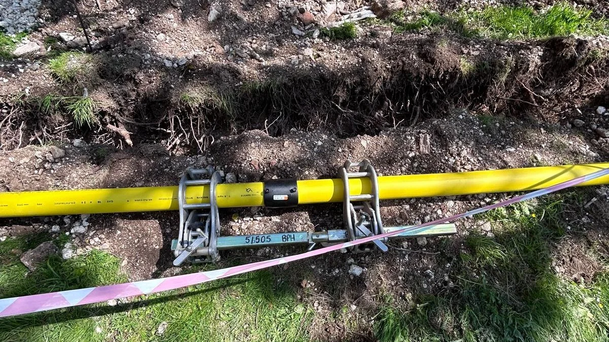 Yellow gas main laid in an open trench with barrier tape across a grass verge