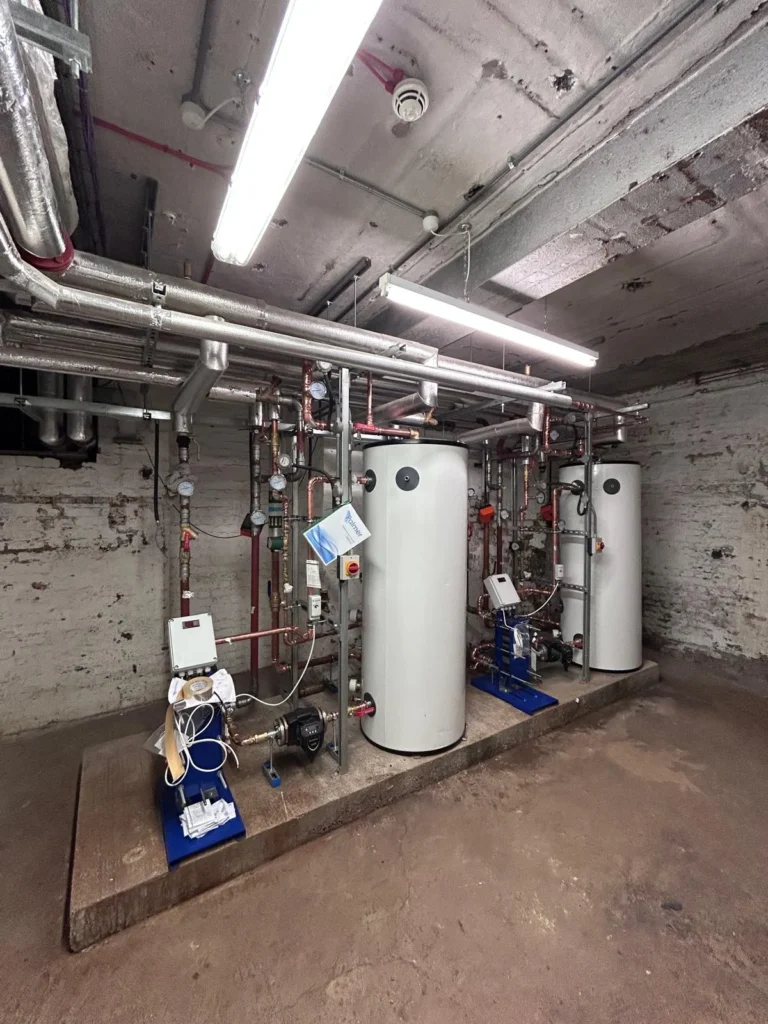 Two unvented cylinders and a pump set mounted on a frame in a brick basement plant room