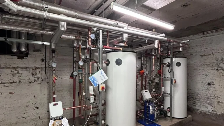 Two unvented cylinders and a pump set mounted on a frame in a brick basement plant room