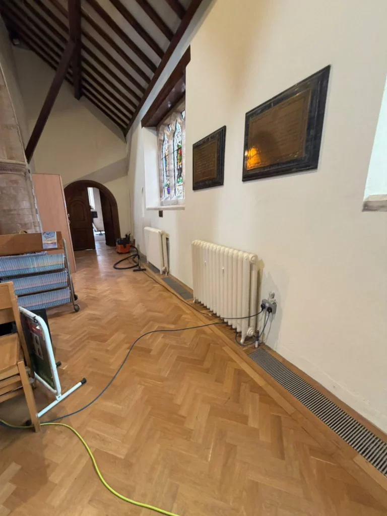 Radiator and heating pipework installed in a commercial hall with a timber floor