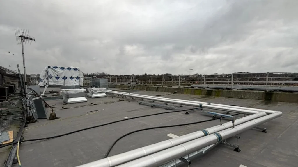Insulated service pipework run across a flat commercial roof on purpose-made supports