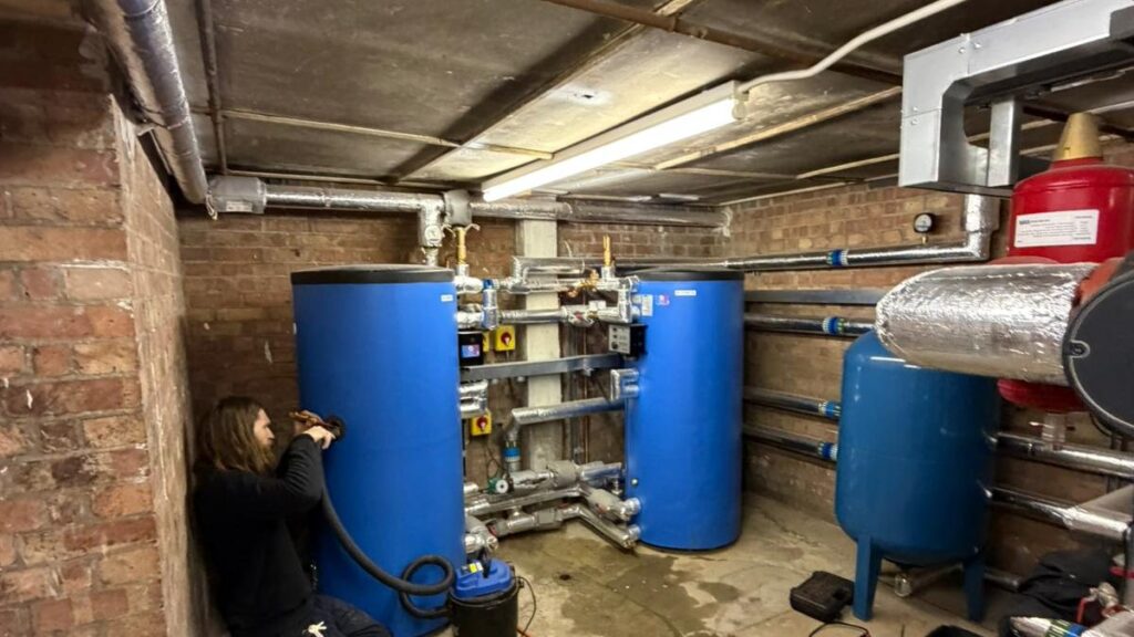Engineer installing pressure vessels, plate heat exchanger and pipework in a commercial plant room
