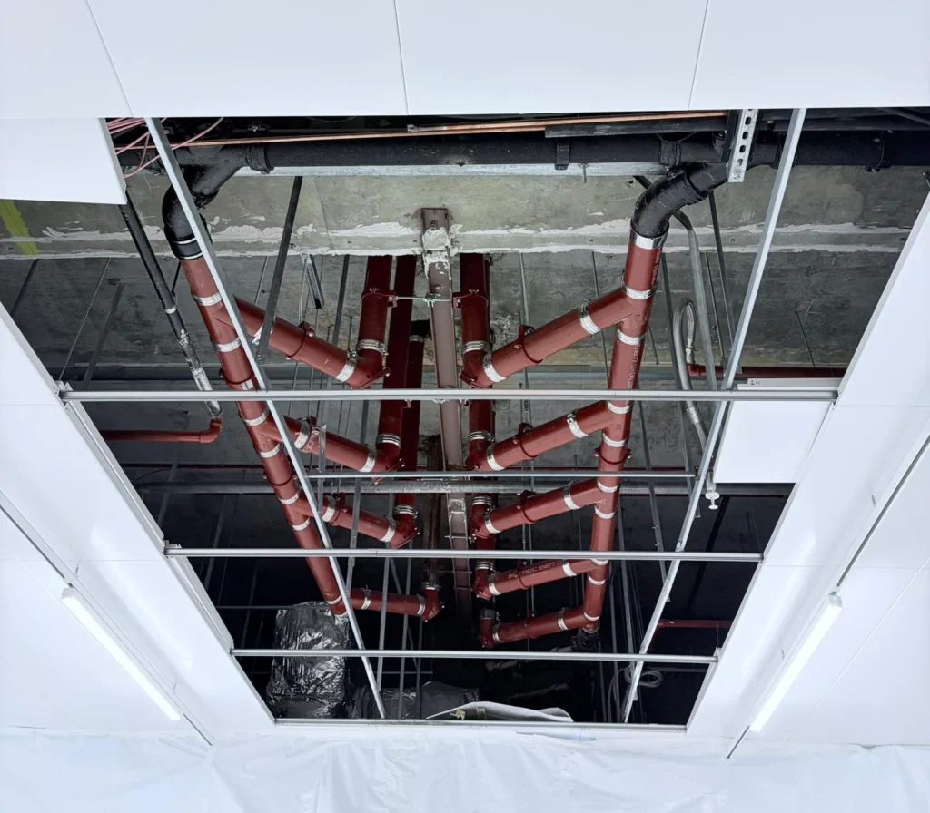 Painted steel service pipework and supports installed above a suspended ceiling grid