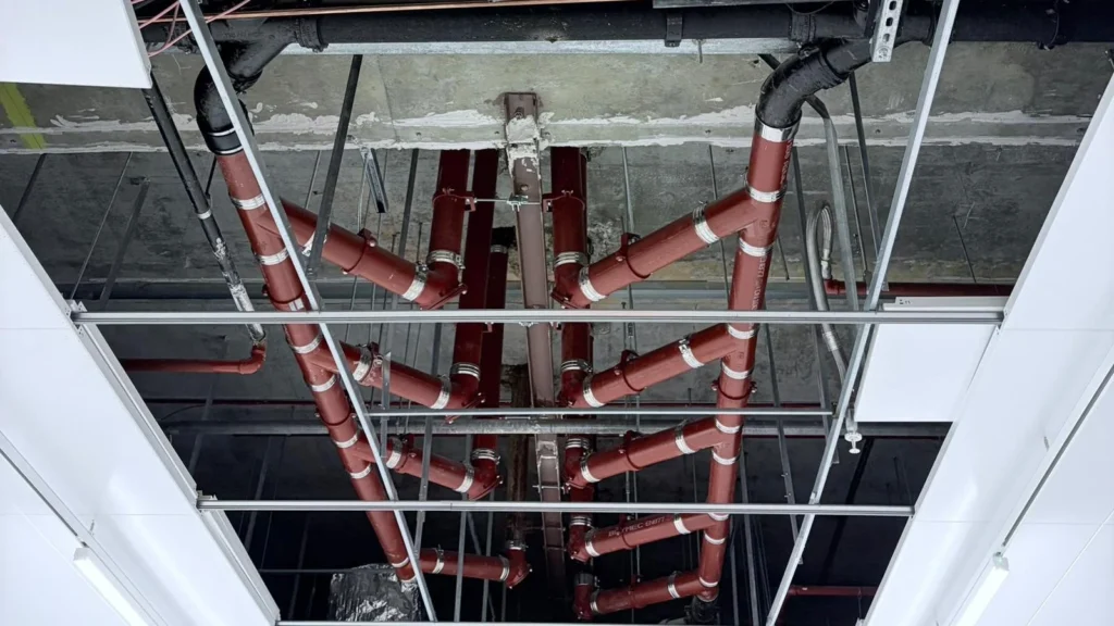 Painted steel service pipework and supports installed above a suspended ceiling grid