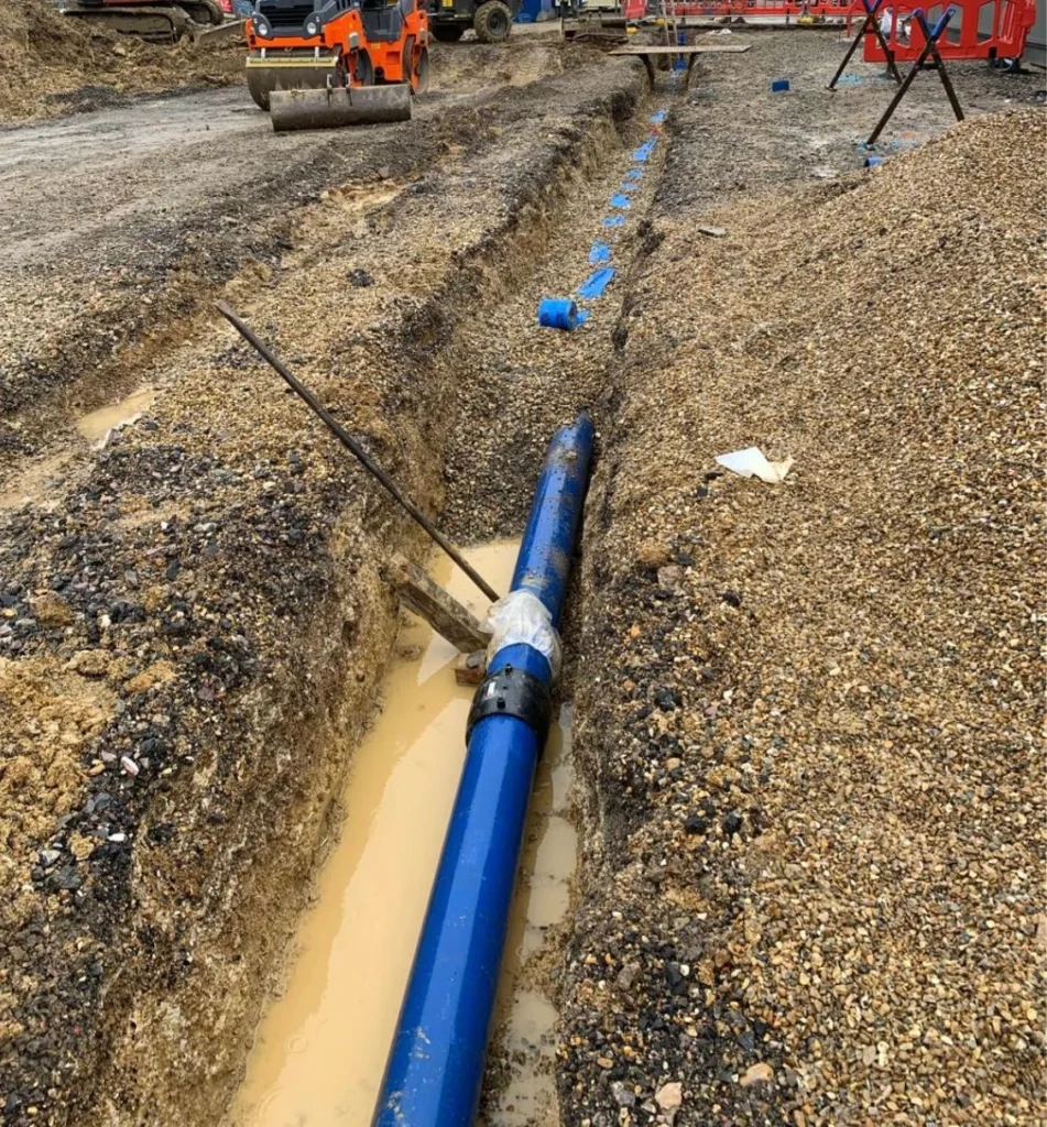 Blue water main laid in a long trench across a site with plant working in the background