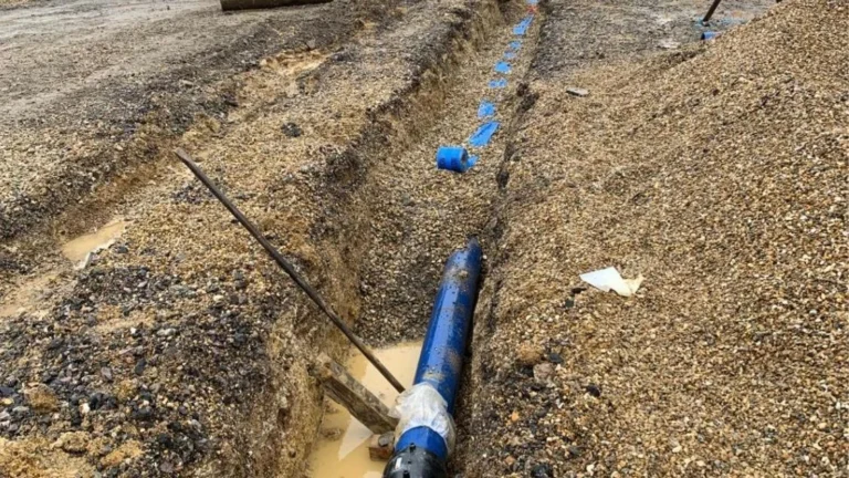 Blue water main laid in a long trench across a site with plant working in the background