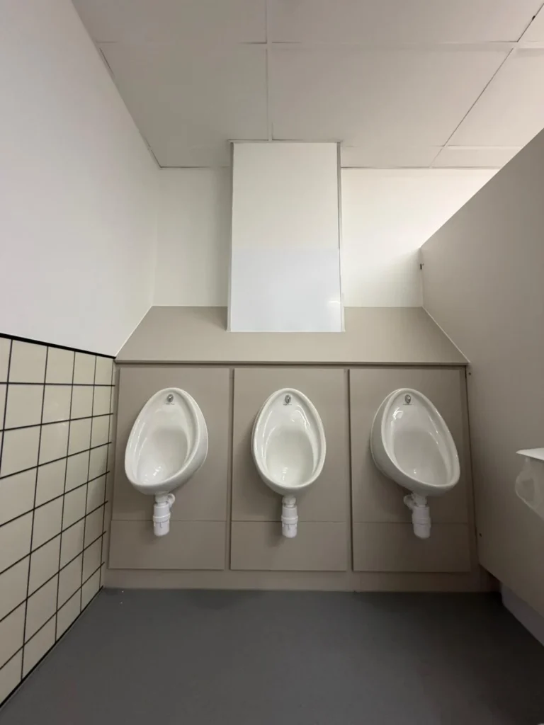 Wall-hung urinals and concealed pipework in a completed commercial washroom