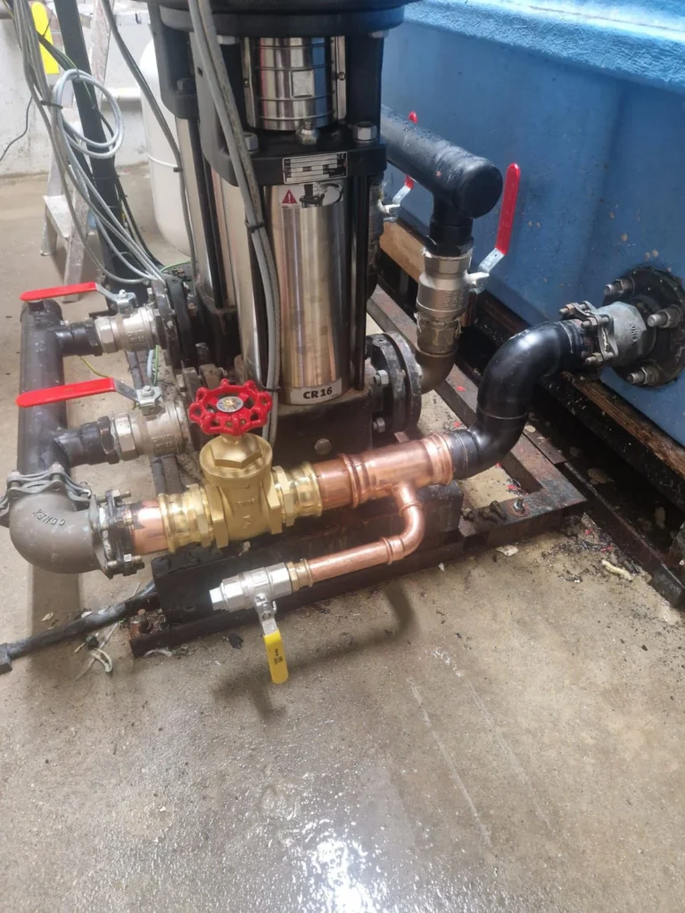Booster pump with brass isolation valves and copper pipework alongside a storage tank