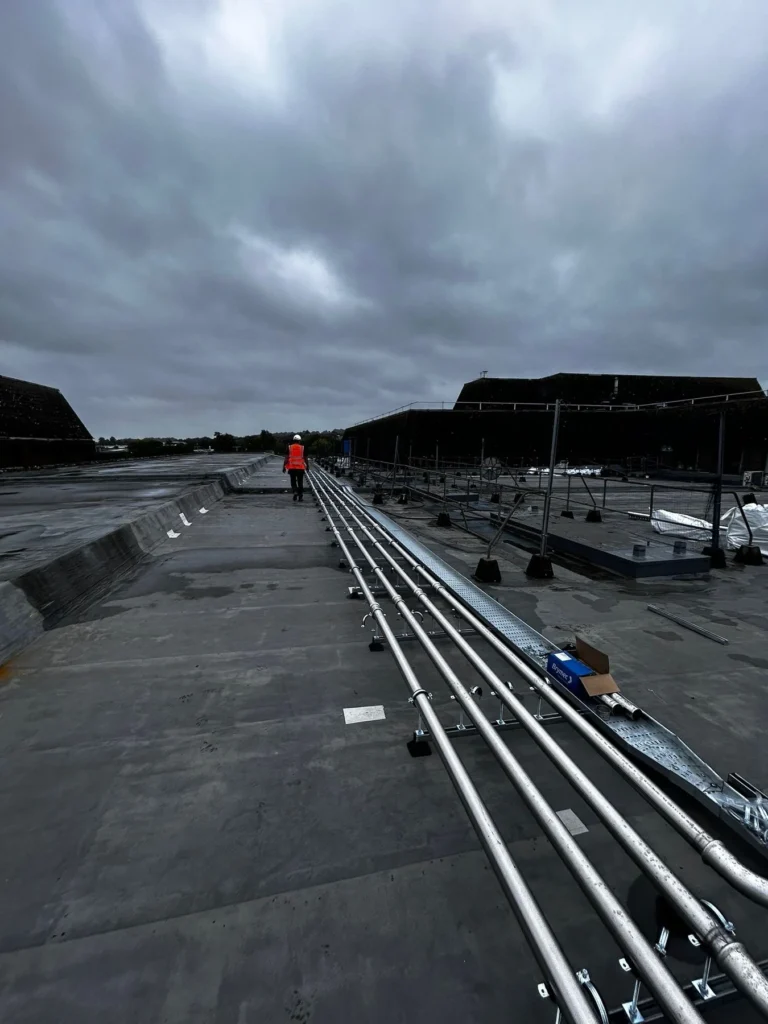 Engineer in high visibility clothing walking beside a rooftop pipework installation