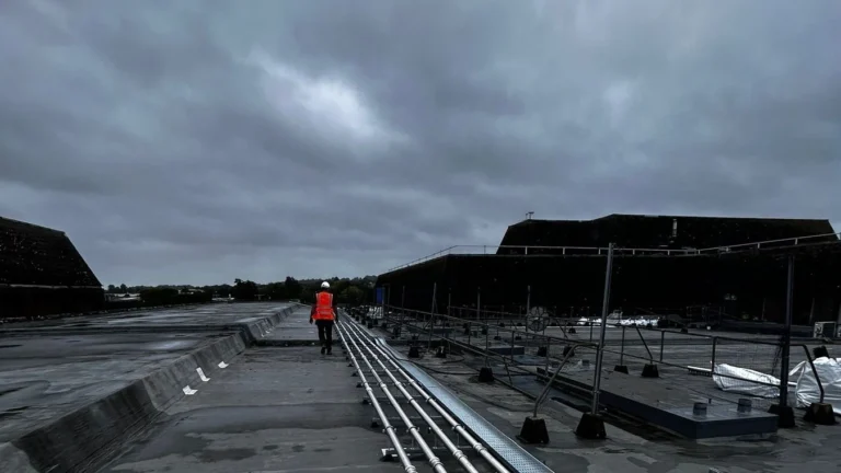Engineer in high visibility clothing walking beside a rooftop pipework installation