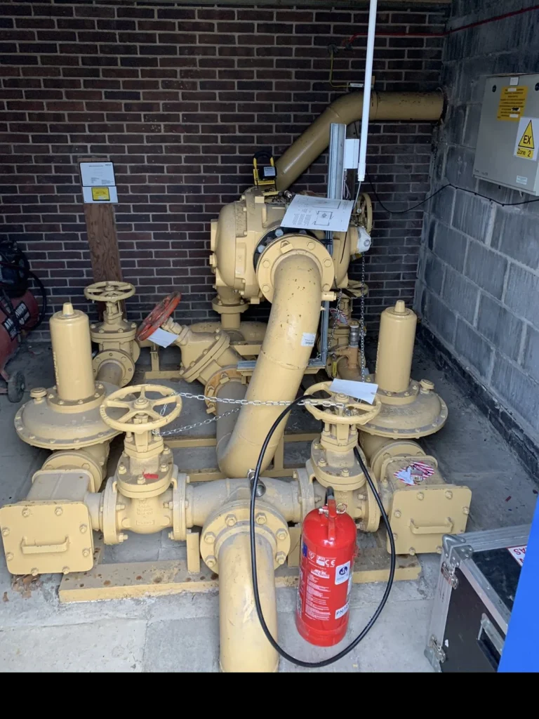 Yellow gas meter, regulator and valve set in an external brick housing during an annual tightness test