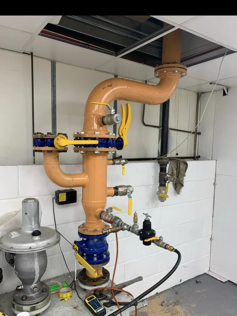 Orange gas supply pipework to a spray booth with butterfly valve, governor and test point connected for tightness testing